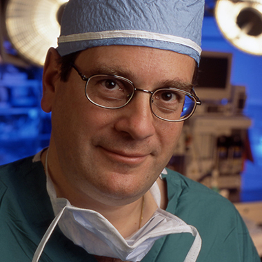 Neurosurgeon Henry Brem in a formal portrait in an operating room wearing scrubs and a surgical cap.