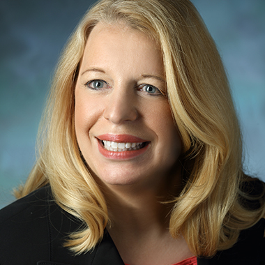 Mindy Christianson, in a formal portrait, wearing a black jacket and red shirt