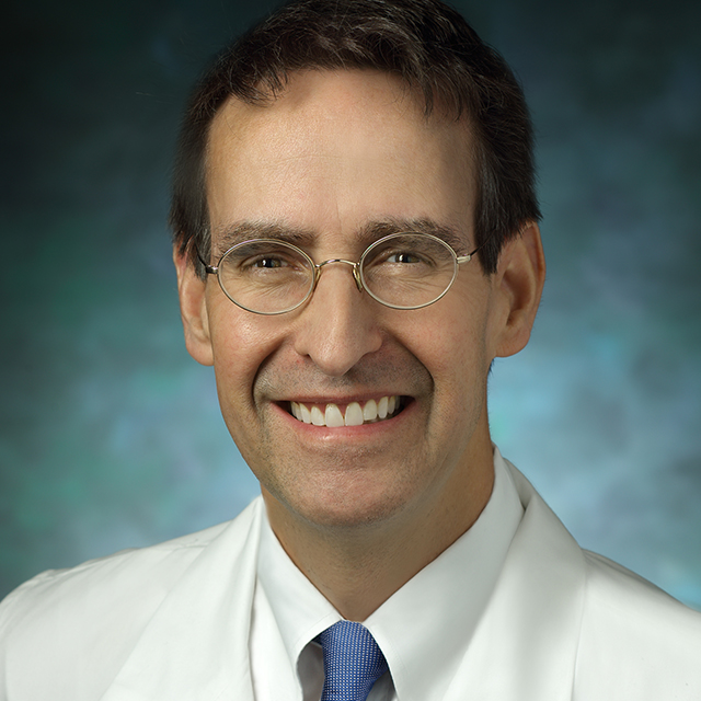 James Gammie, in a formal portrait, wearing a white lab coat, white button down shirt and blue tie. 