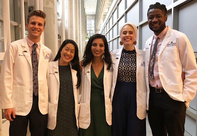 A group of students smile, wearing white coats
