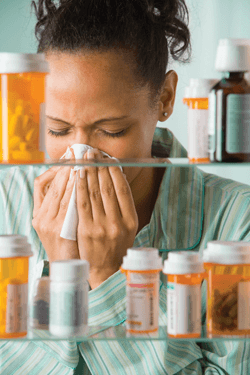 woman blowing her nose and some prescription bottles
