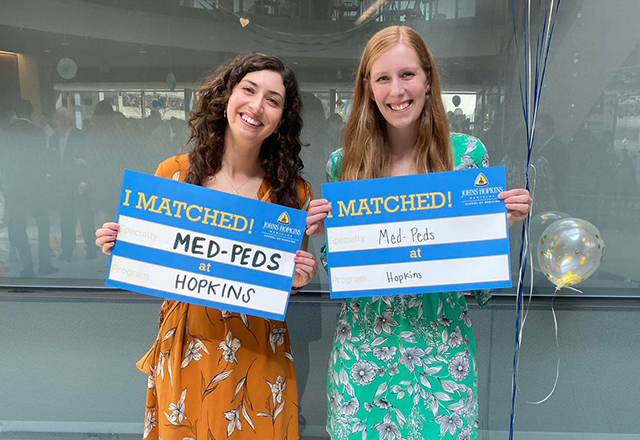 two students holding up a sign that they matched with the program