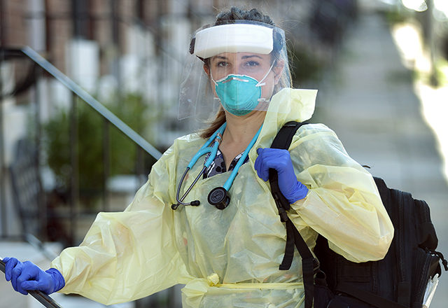 Amy Kilen, wearing protective equipment, stands on the front steps of a rowhouse. A backpack is slung over her shoulder.