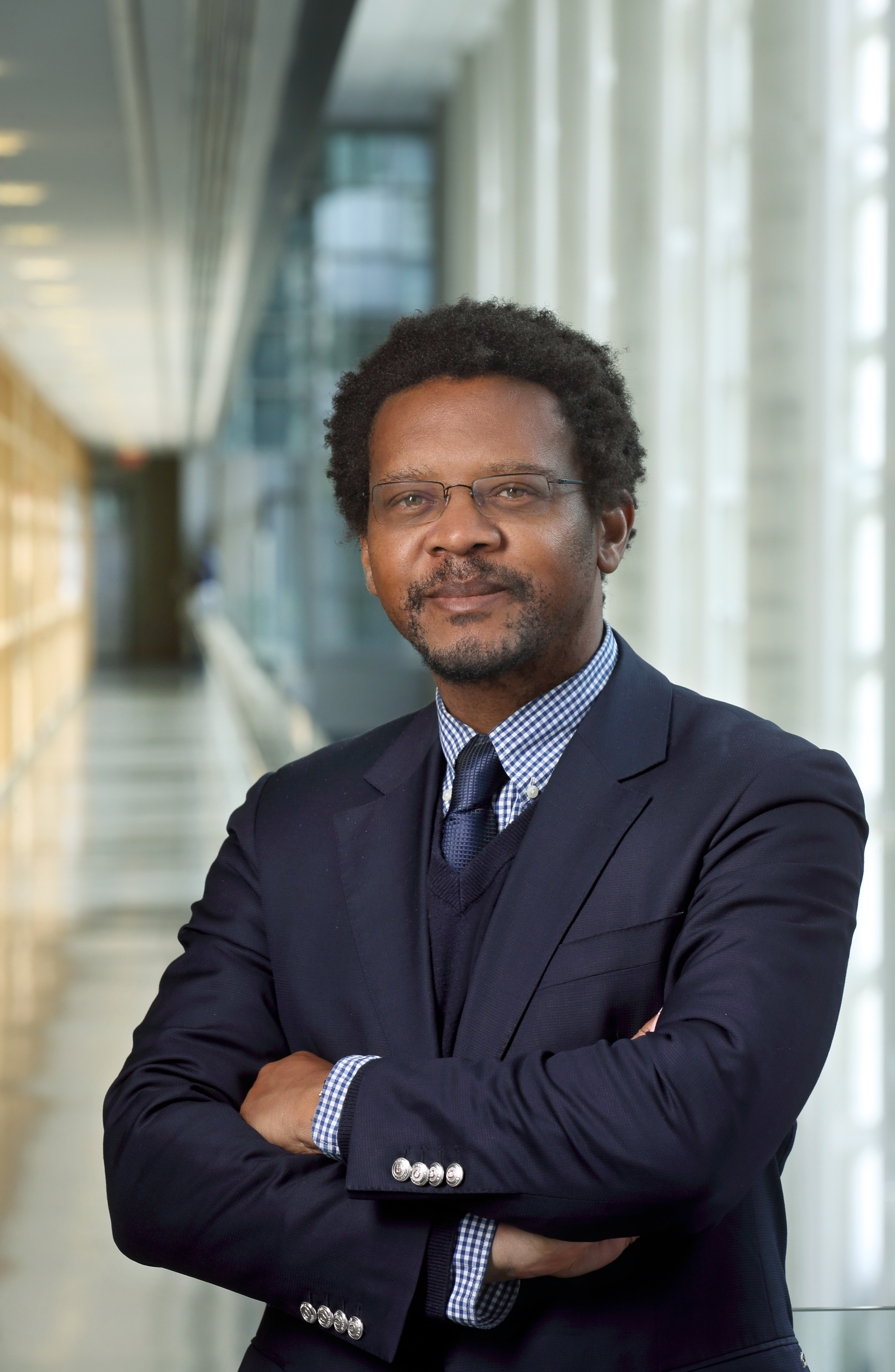 Portrait photo of Ambroise Wonkam, director, department of genetic medicine. He is An african american man standing in the hallway of a research building