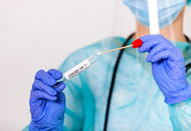 A healthcare working holding up a test tube and cotton swab.