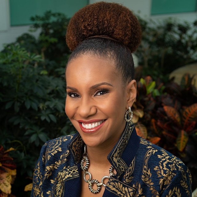 Tonya Matthews in a patterned black and brown blazer, stands in front of a group of plants.