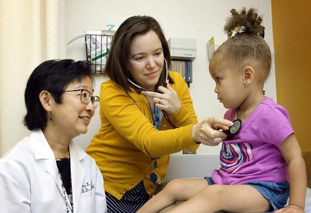 physician and resident talking with young girl in doctor's office