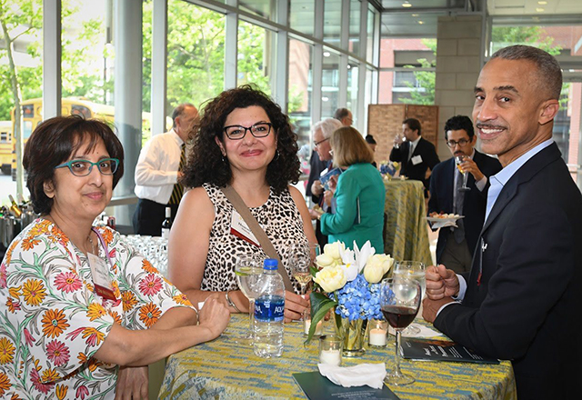 Alumni stand around a table, socializing at an event.