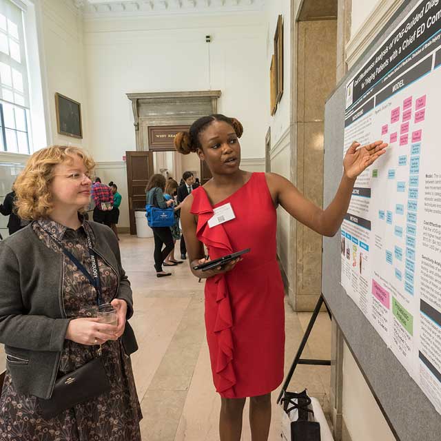 doctoral student Maningbè Keita points to a poster showing her study about stroke diagnosis, as pathologist Jody Hooper looks and listens. 