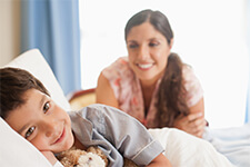 Un niño en una cama del hospital sonríe mientras su madre le cuida