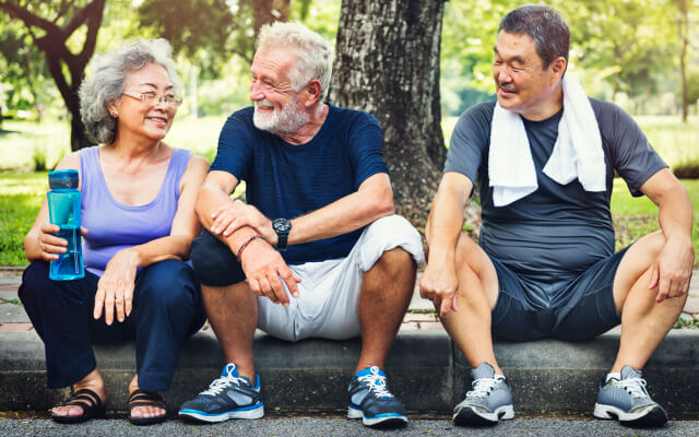 A group of three active seniors sitting on a curb after an exercise