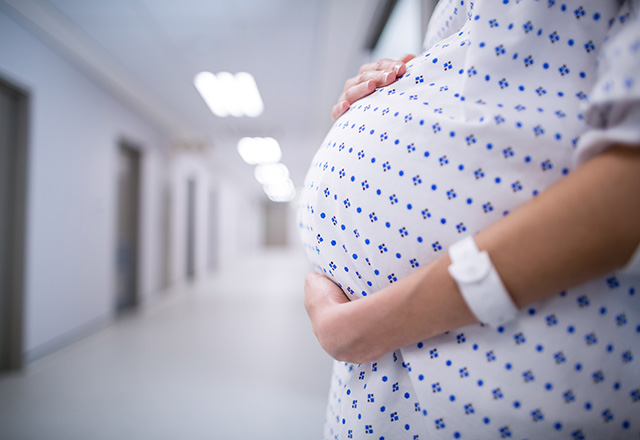A pregnant woman wearing a hospital gown cradles her stomach.