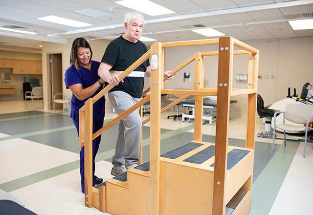 a therapist helps a patient walk up stairs in a rehab gym
